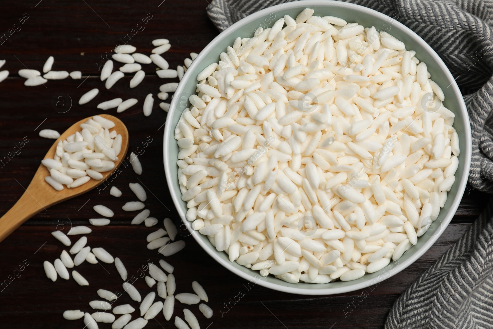 Photo of Puffed rice in bowl and spoon on wooden table, flat lay