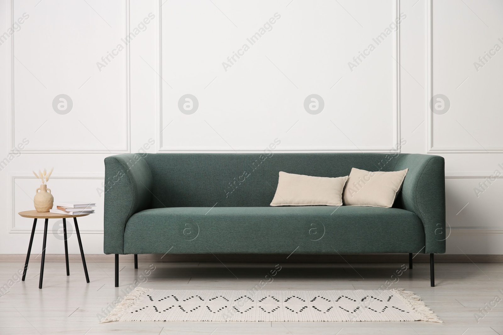 Photo of Stylish sofa, pillows and side table with decor near white wall indoors