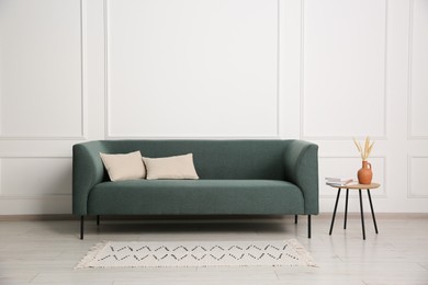 Photo of Stylish sofa, pillows and side table with decor near white wall indoors