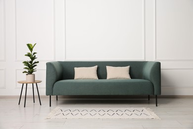 Photo of Stylish sofa, pillows and side table with houseplant near white wall indoors