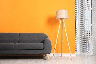 Photo of Stylish sofa and lamp near orange wall indoors