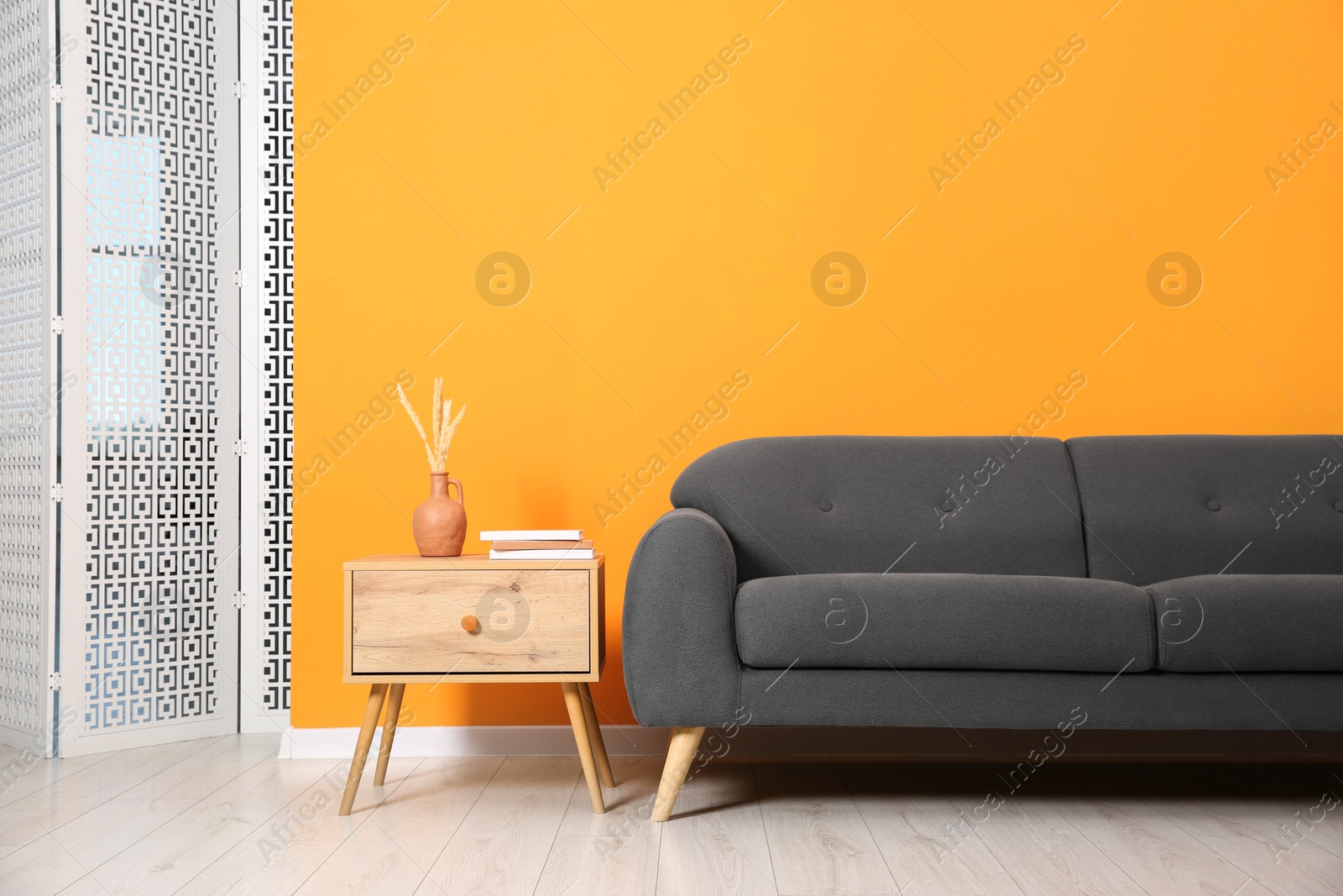 Photo of Stylish sofa and side table with decor near orange wall indoors