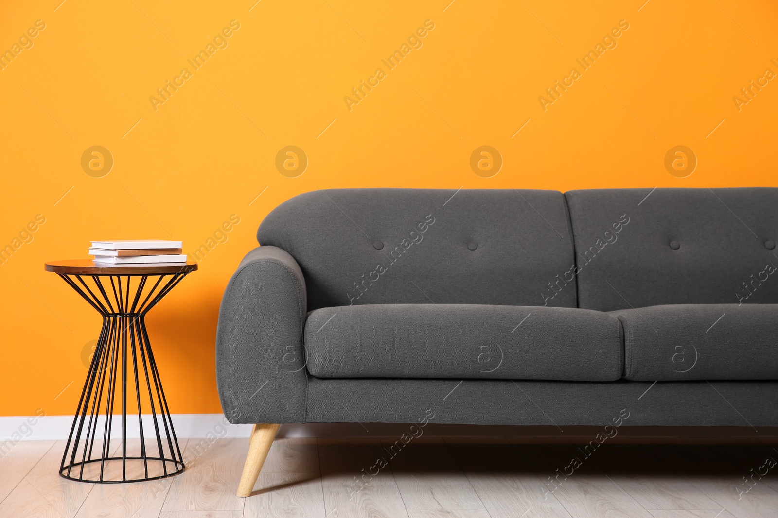 Photo of Stylish sofa and side table with books near orange wall indoors