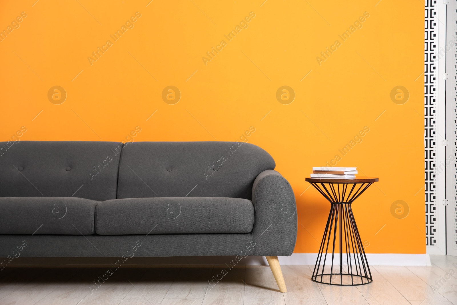 Photo of Stylish sofa and side table with books near orange wall indoors