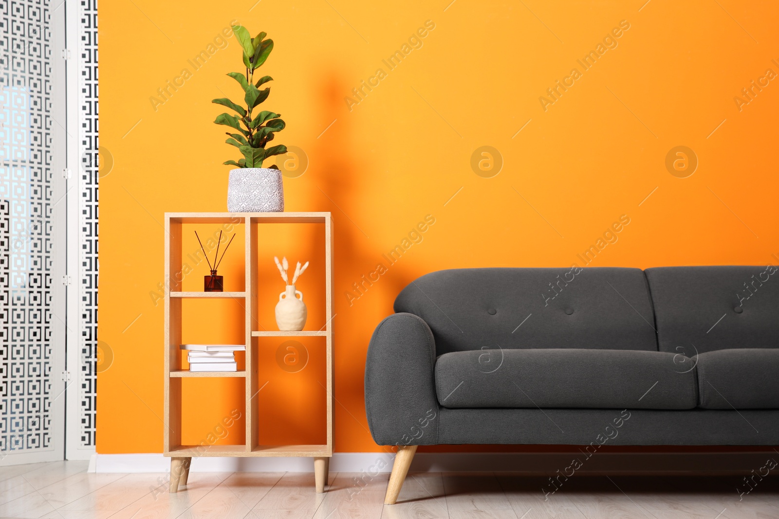 Photo of Stylish sofa and shelving unit with decor near orange wall indoors