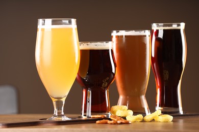 Photo of Glasses with different types of beer and snacks on wooden table indoors, closeup