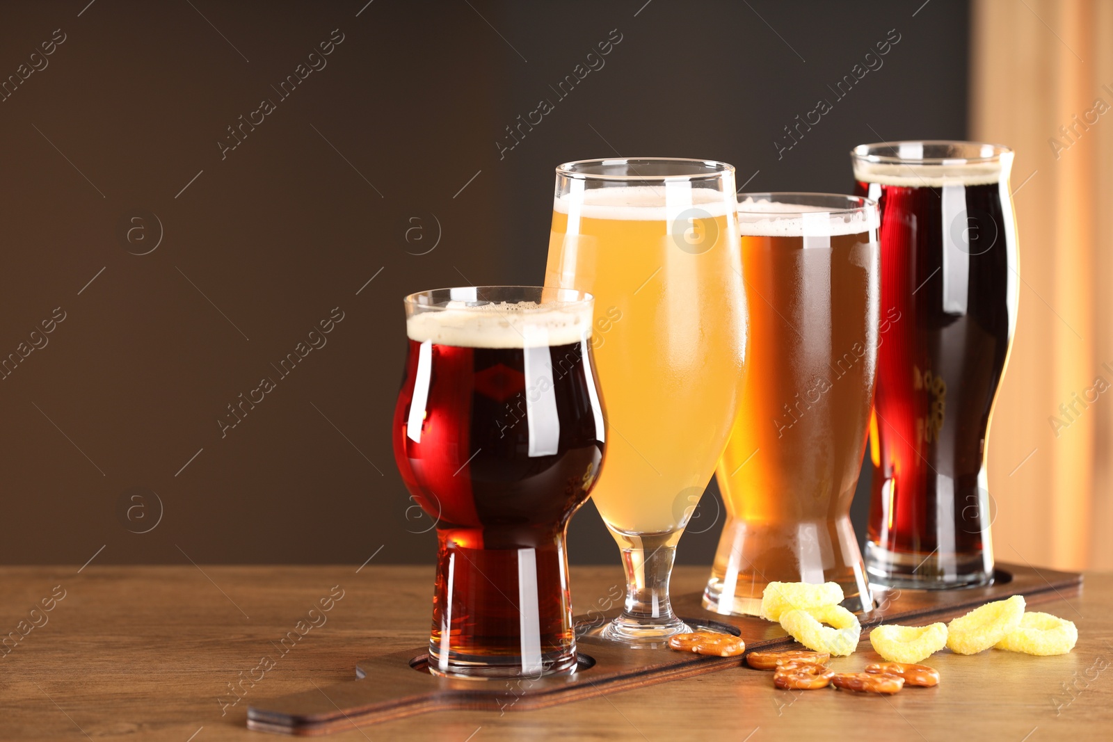 Photo of Glasses with different types of beer and snacks on wooden table indoors, space for text