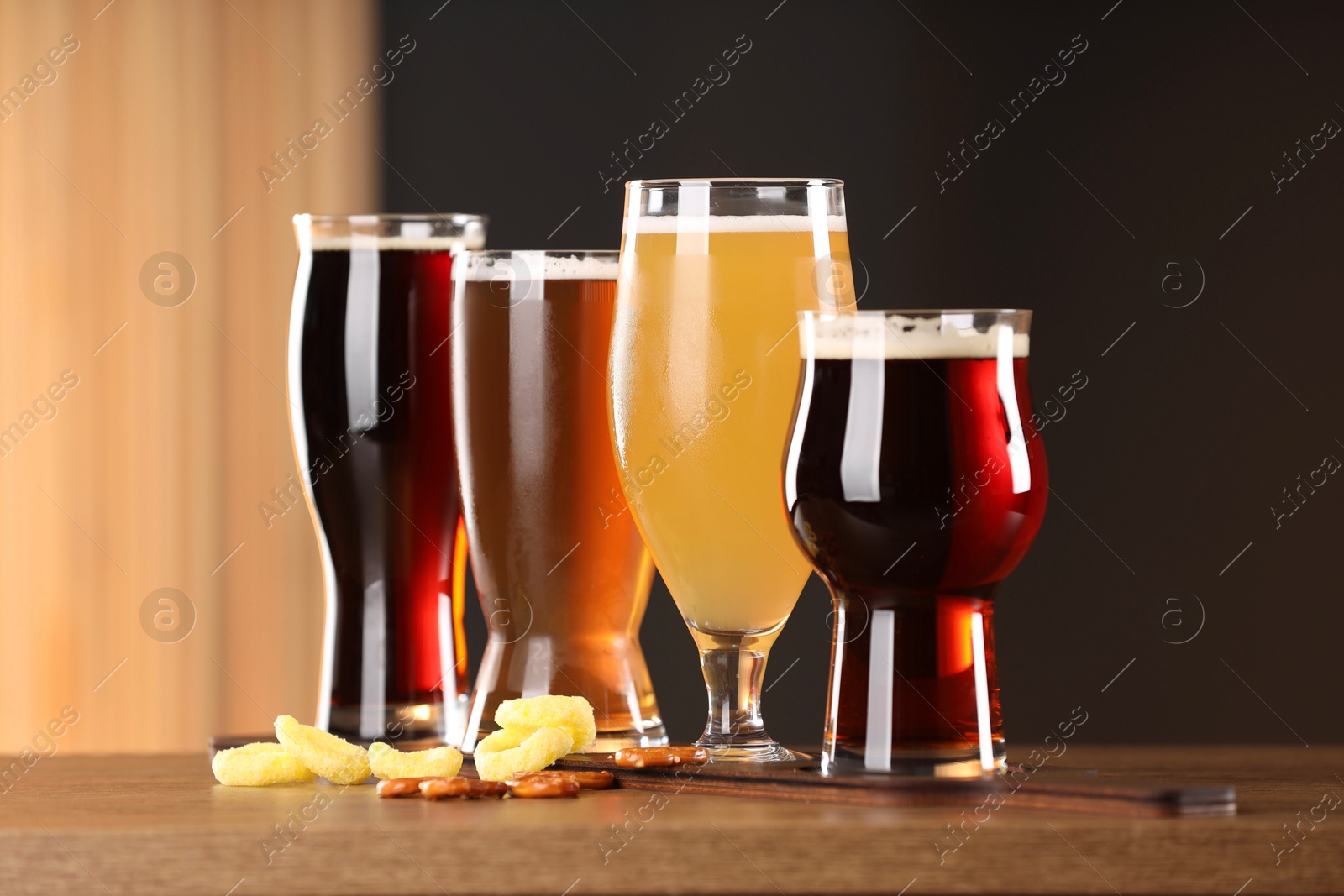 Photo of Glasses with different types of beer and snacks on wooden table indoors