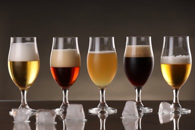 Photo of Glasses with different types of beer and ice cubes on mirror surface