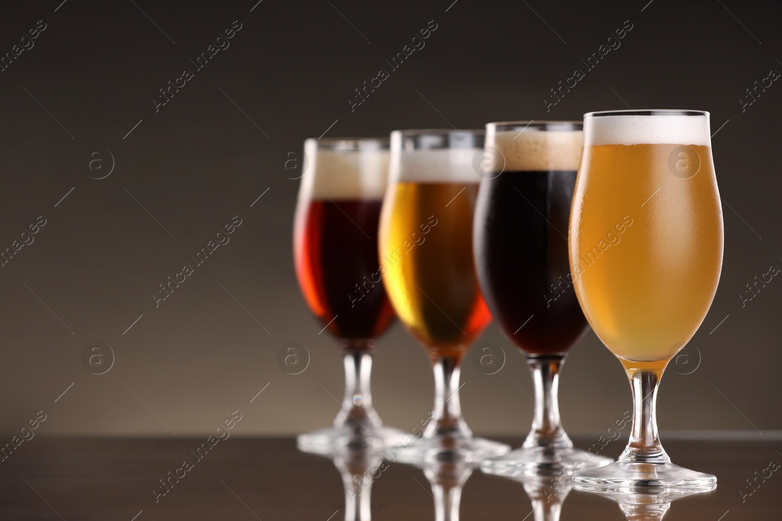 Photo of Glasses with different types of beer on mirror surface, closeup. Space for text