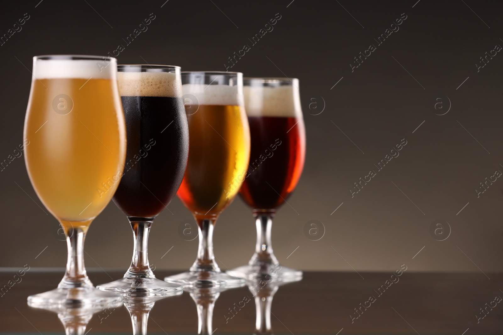 Photo of Glasses with different types of beer on mirror surface, closeup. Space for text