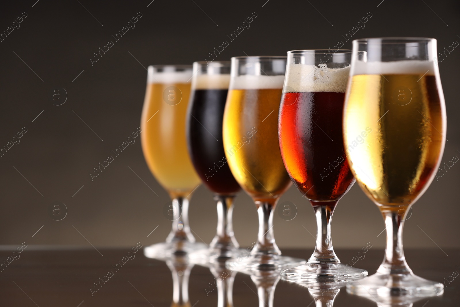 Photo of Glasses with different types of beer on mirror surface, closeup. Space for text