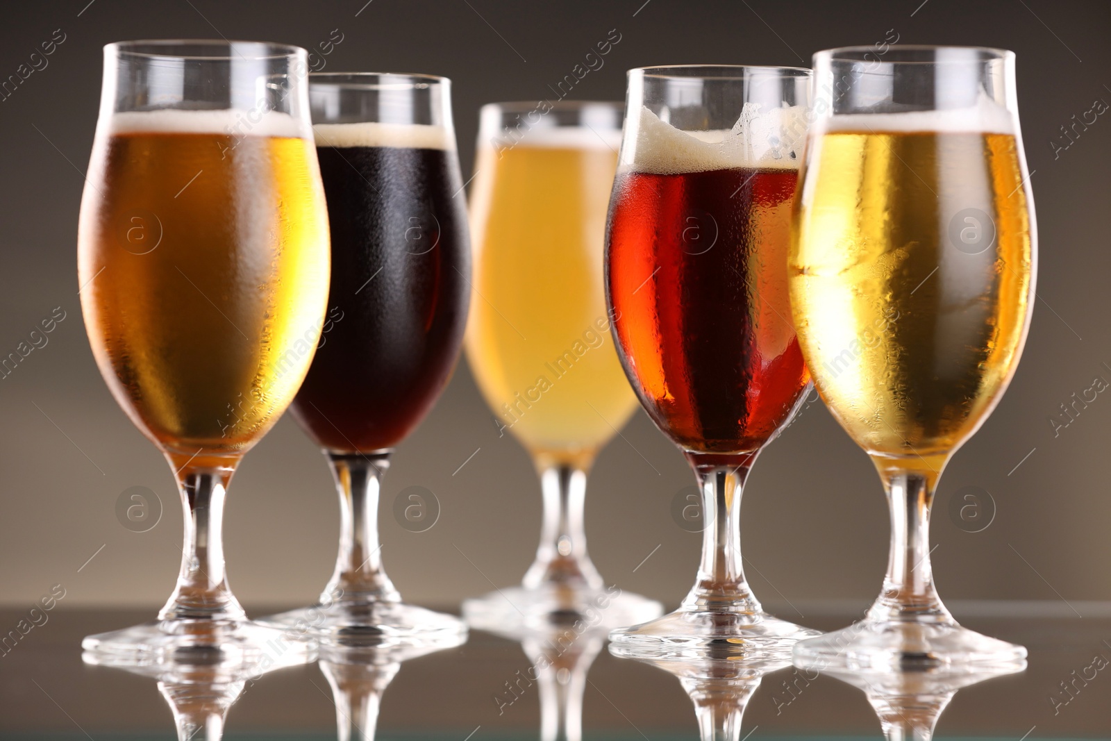 Photo of Glasses with different types of beer on mirror surface, closeup