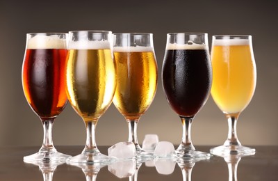 Photo of Glasses with different types of beer and ice cubes on mirror surface, closeup