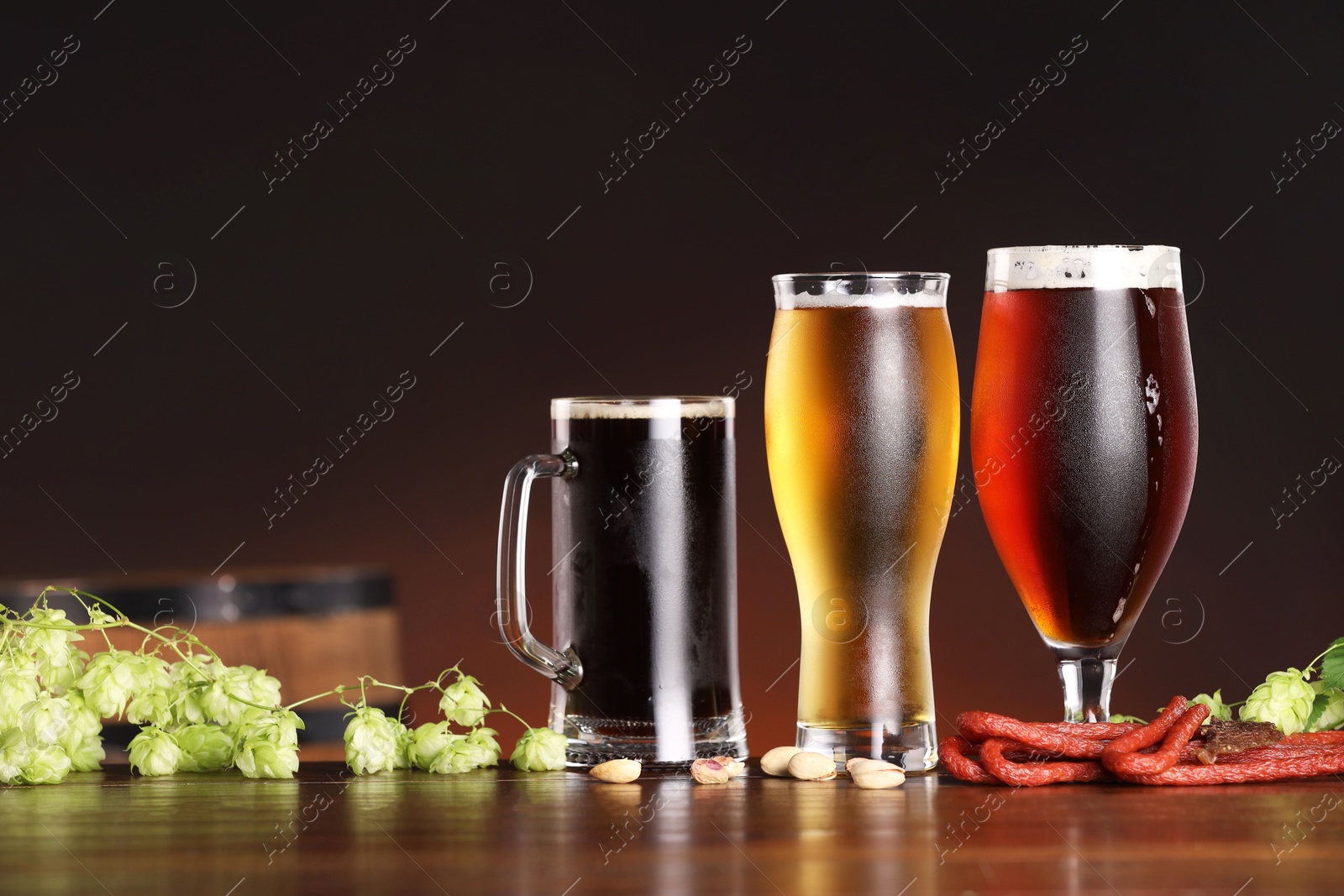 Photo of Glasses with different types of beer, snacks and fresh hops on wooden table in bar