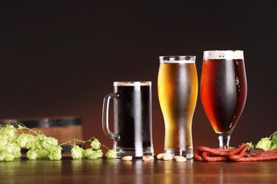 Photo of Glasses with different types of beer, snacks and fresh hops on wooden table in bar