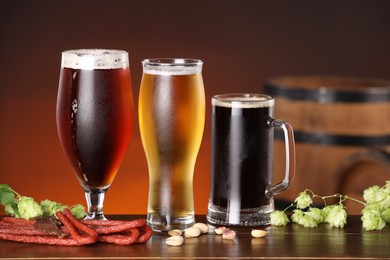 Photo of Glasses with different types of beer, snacks and fresh hops on wooden table in bar