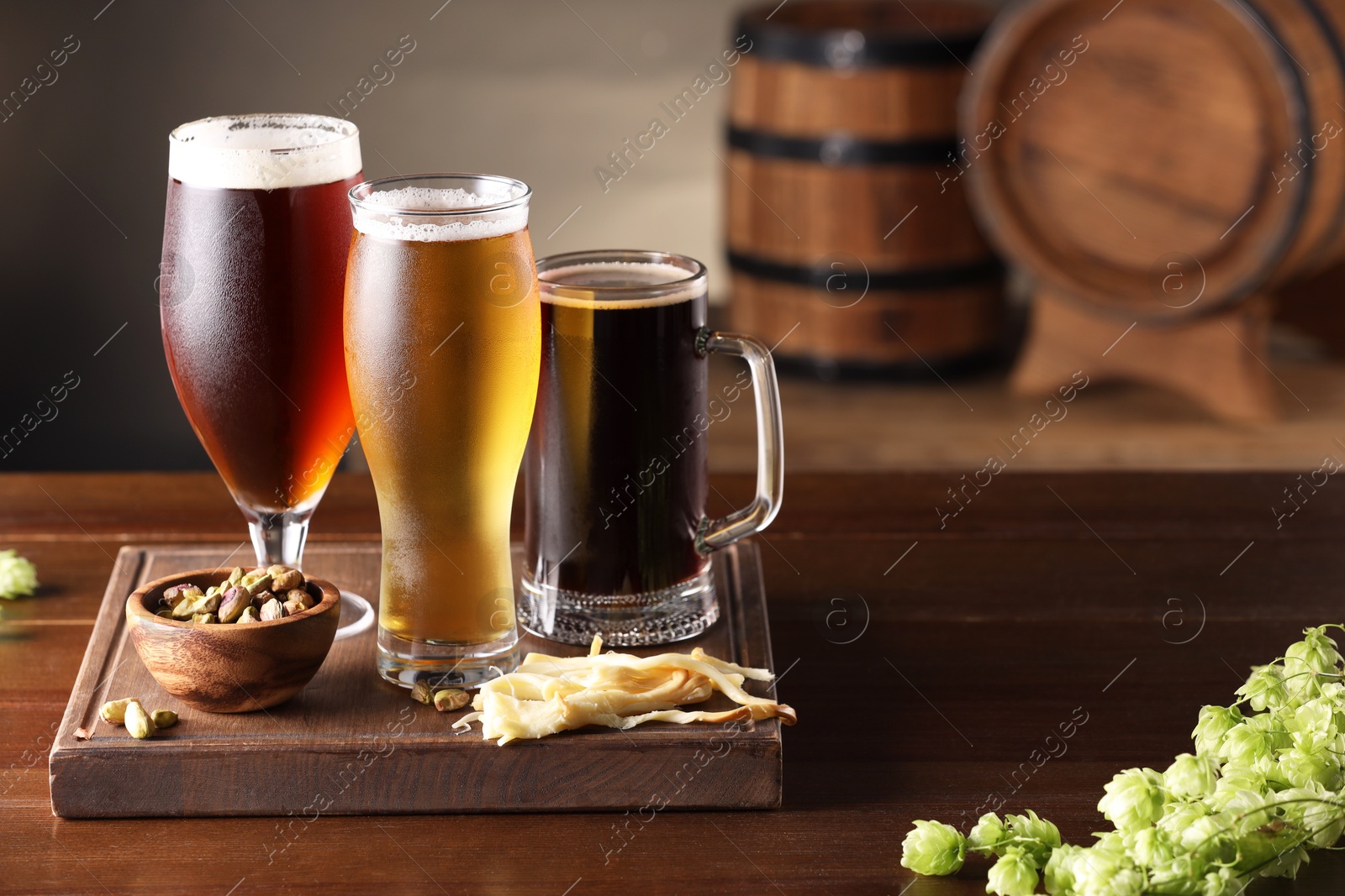 Photo of Glasses with different types of beer, snacks and fresh hops on wooden table in bar