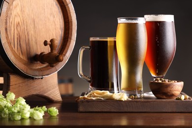 Photo of Glasses with different types of beer, barrel, snacks and fresh hops on wooden table