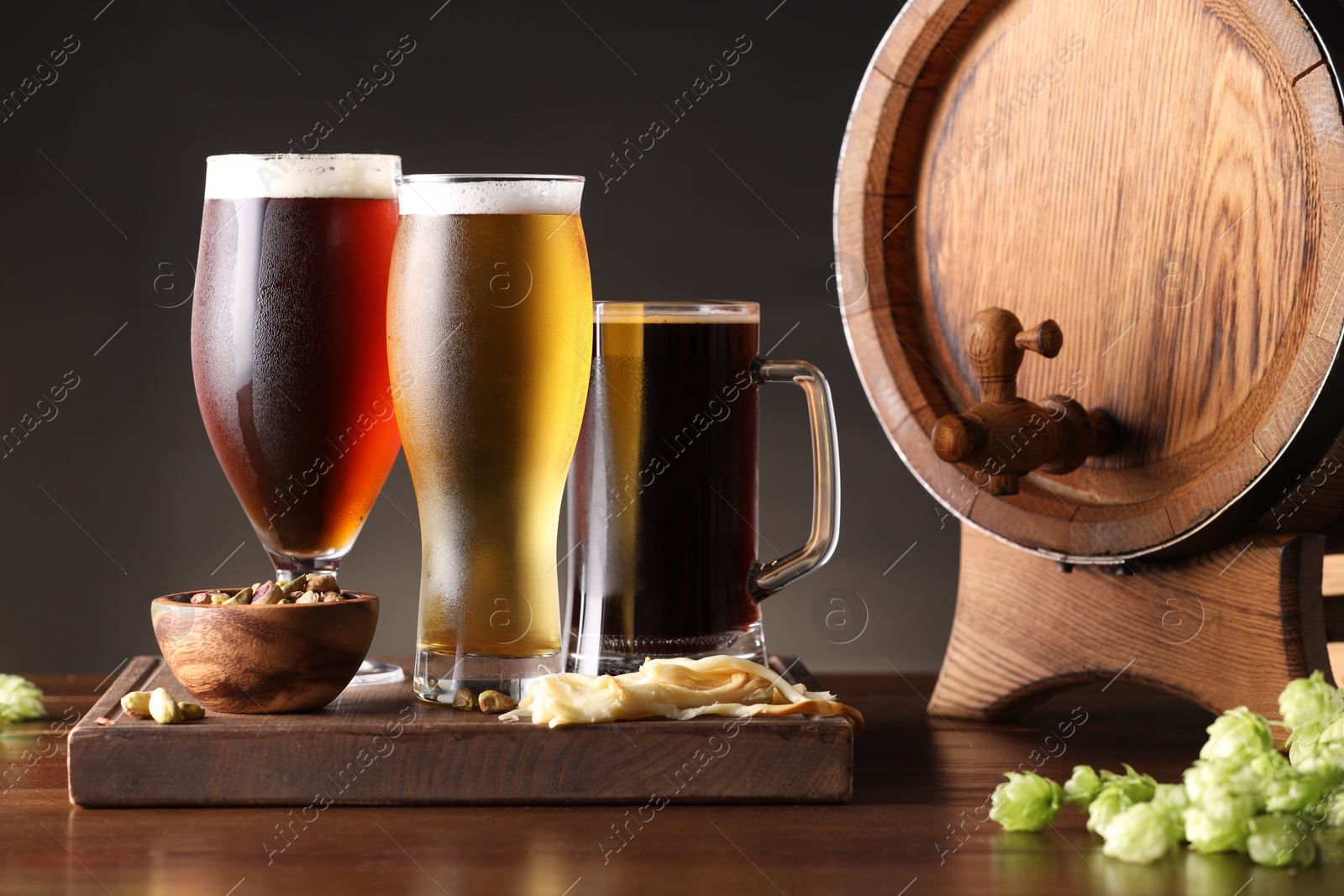 Photo of Glasses with different types of beer, barrel, snacks and fresh hops on wooden table