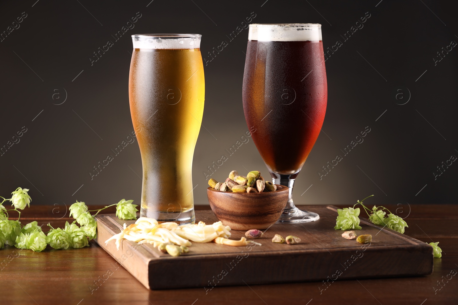 Photo of Glasses with different types of beer, snacks and fresh hops on wooden table