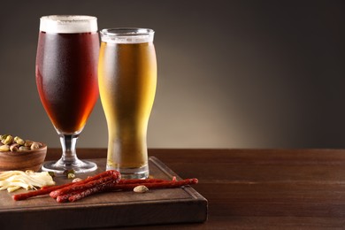 Photo of Glasses with different types of beer and snacks on wooden table, closeup. Space for text