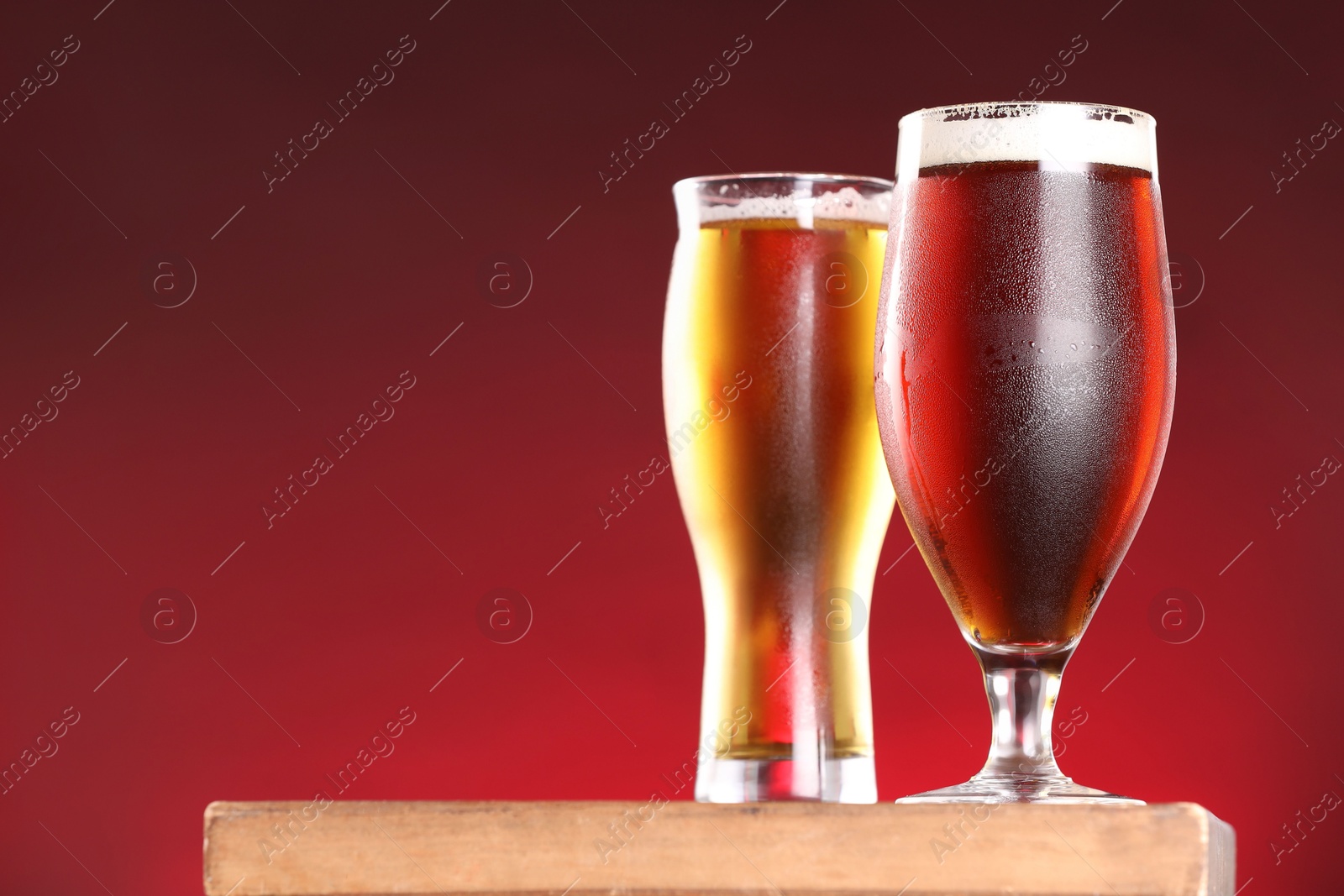 Photo of Glasses with different types of beer on board against red background, closeup. Space for text