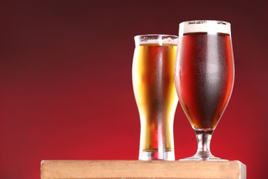 Photo of Glasses with different types of beer on board against red background, closeup. Space for text