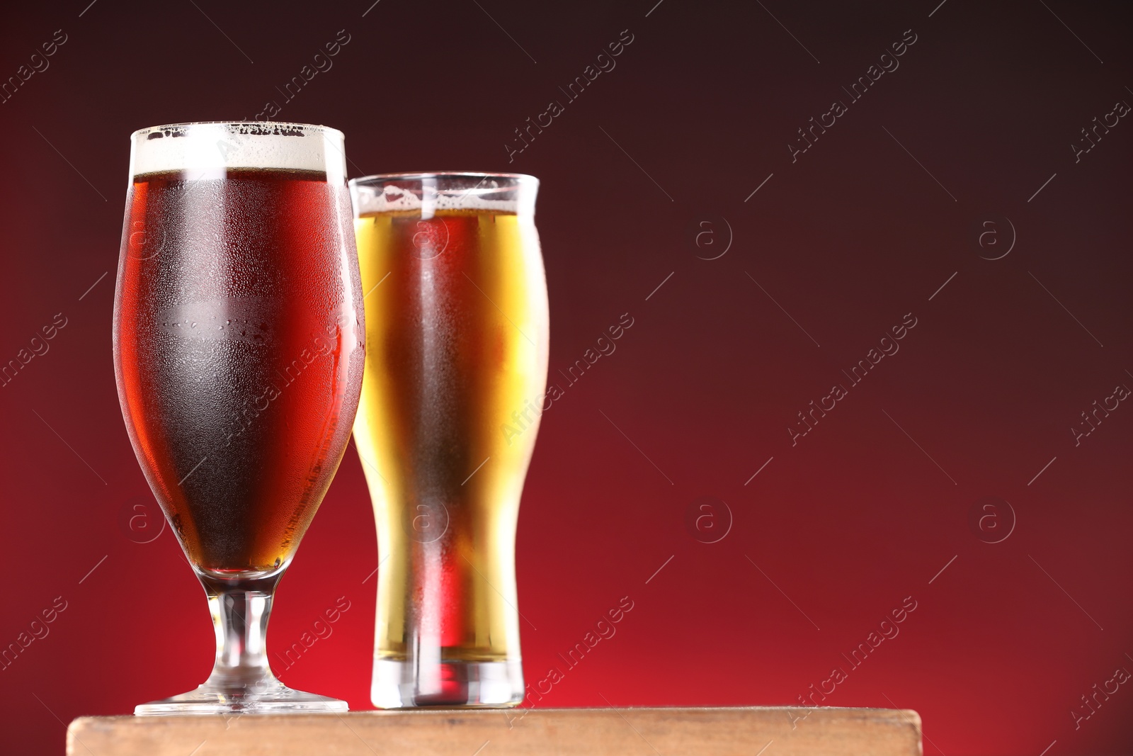 Photo of Glasses with different types of beer on board against red background, closeup. Space for text