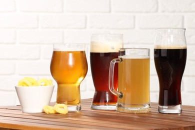 Photo of Glasses with different types of beer and snacks on wooden table against white brick wall