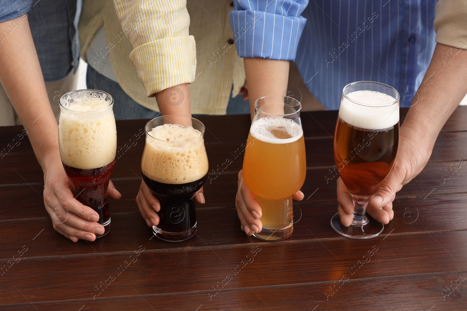 Photo of People with different types of beer in glasses at wooden table, closeup