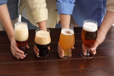 Photo of People with different types of beer in glasses at wooden table, closeup