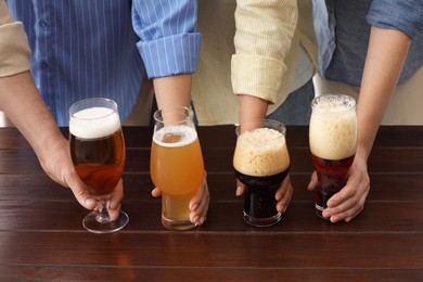 Photo of People with different types of beer in glasses at wooden table, closeup