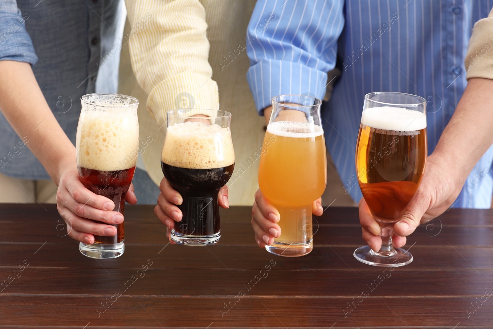 Photo of People with different types of beer in glasses at wooden table, closeup