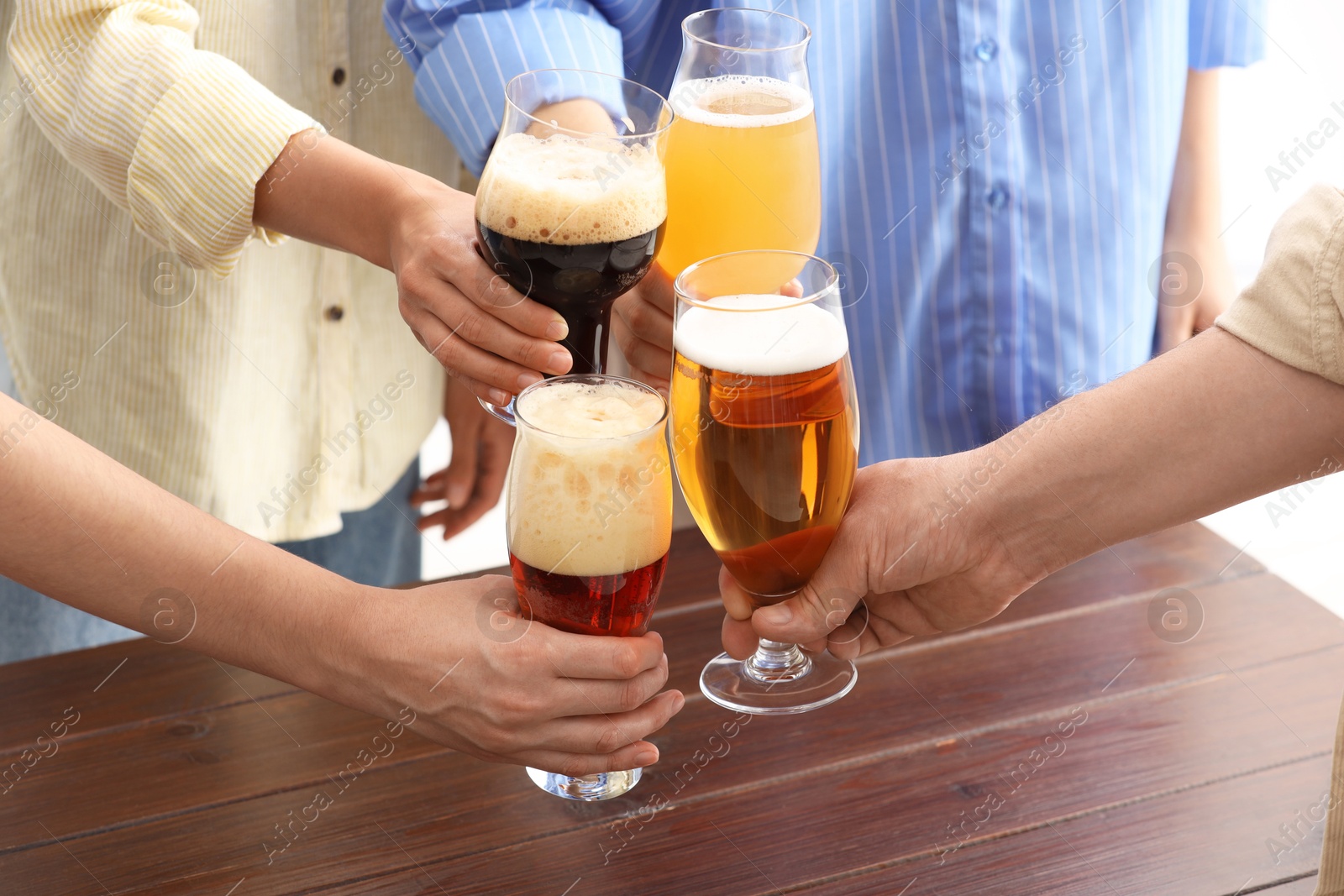 Photo of People with different types of beer clinking glasses at wooden table, closeup