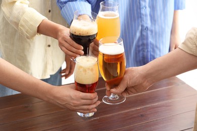 Photo of People with different types of beer clinking glasses at wooden table, closeup