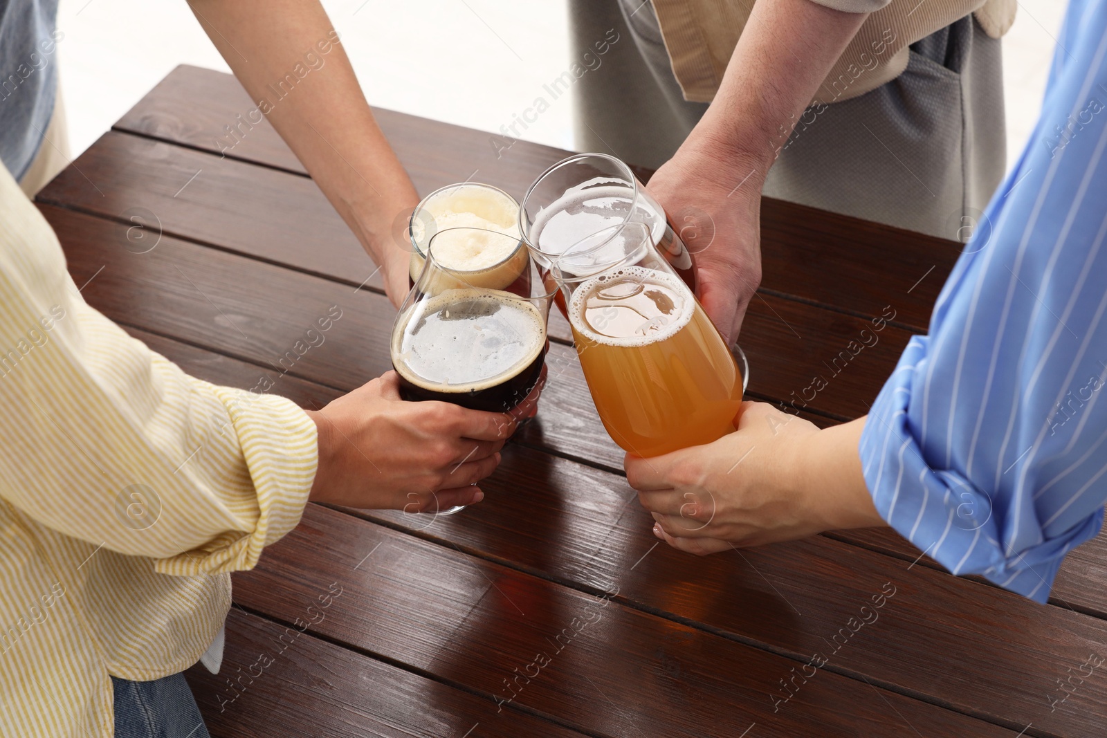 Photo of People with different types of beer clinking glasses at wooden table, closeup