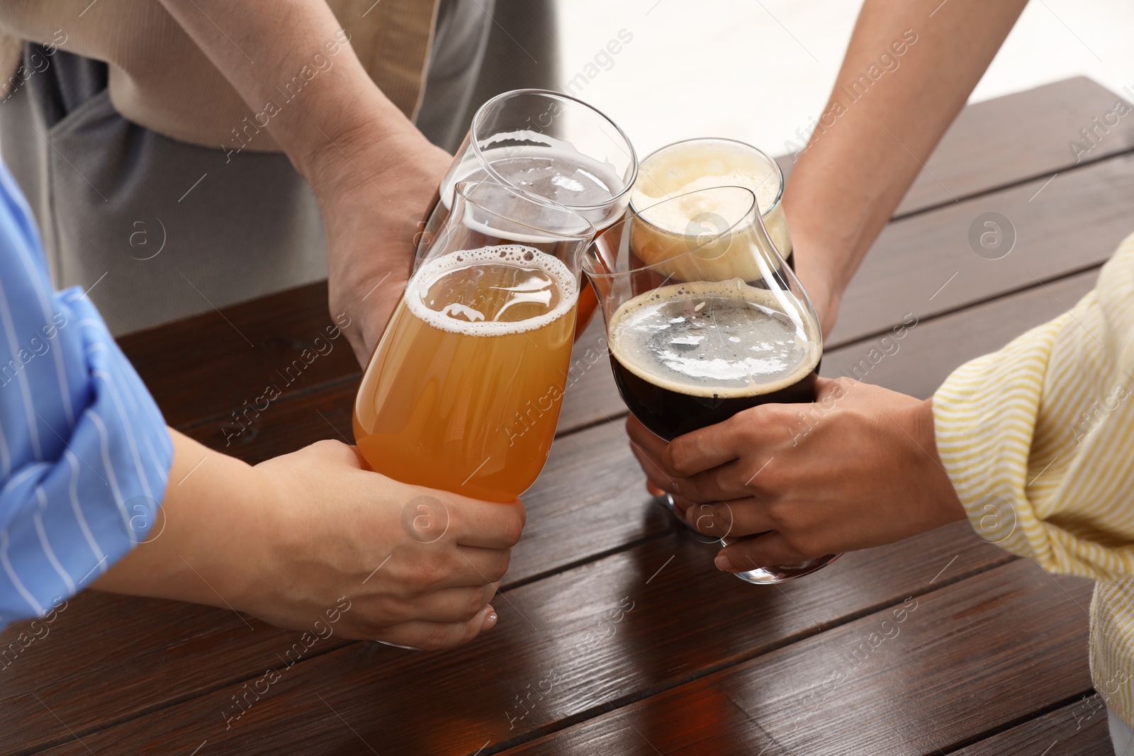 Photo of People with different types of beer clinking glasses at wooden table, closeup