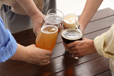 Photo of People with different types of beer clinking glasses at wooden table, closeup