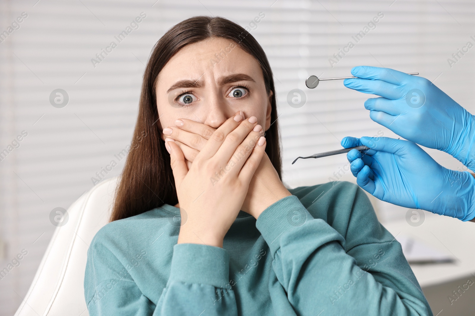 Photo of Dental phobia. Dentist working with scared woman in clinic, closeup