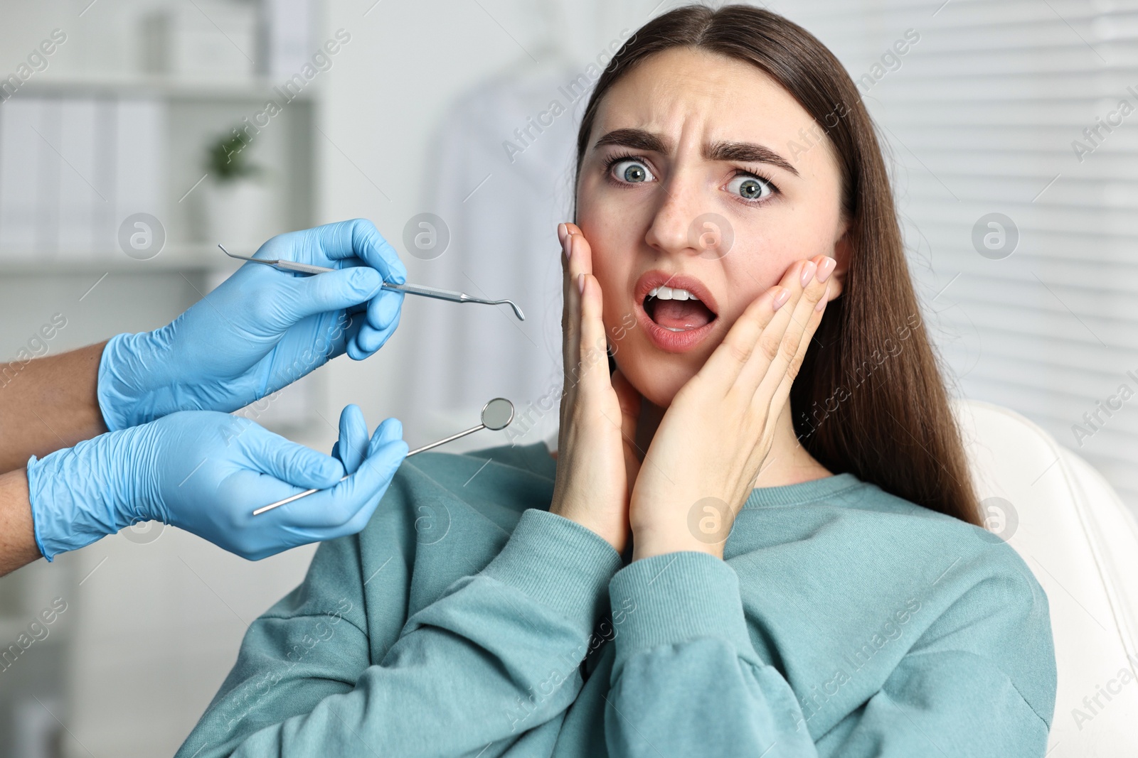 Photo of Dental phobia. Dentist working with scared woman in clinic, closeup