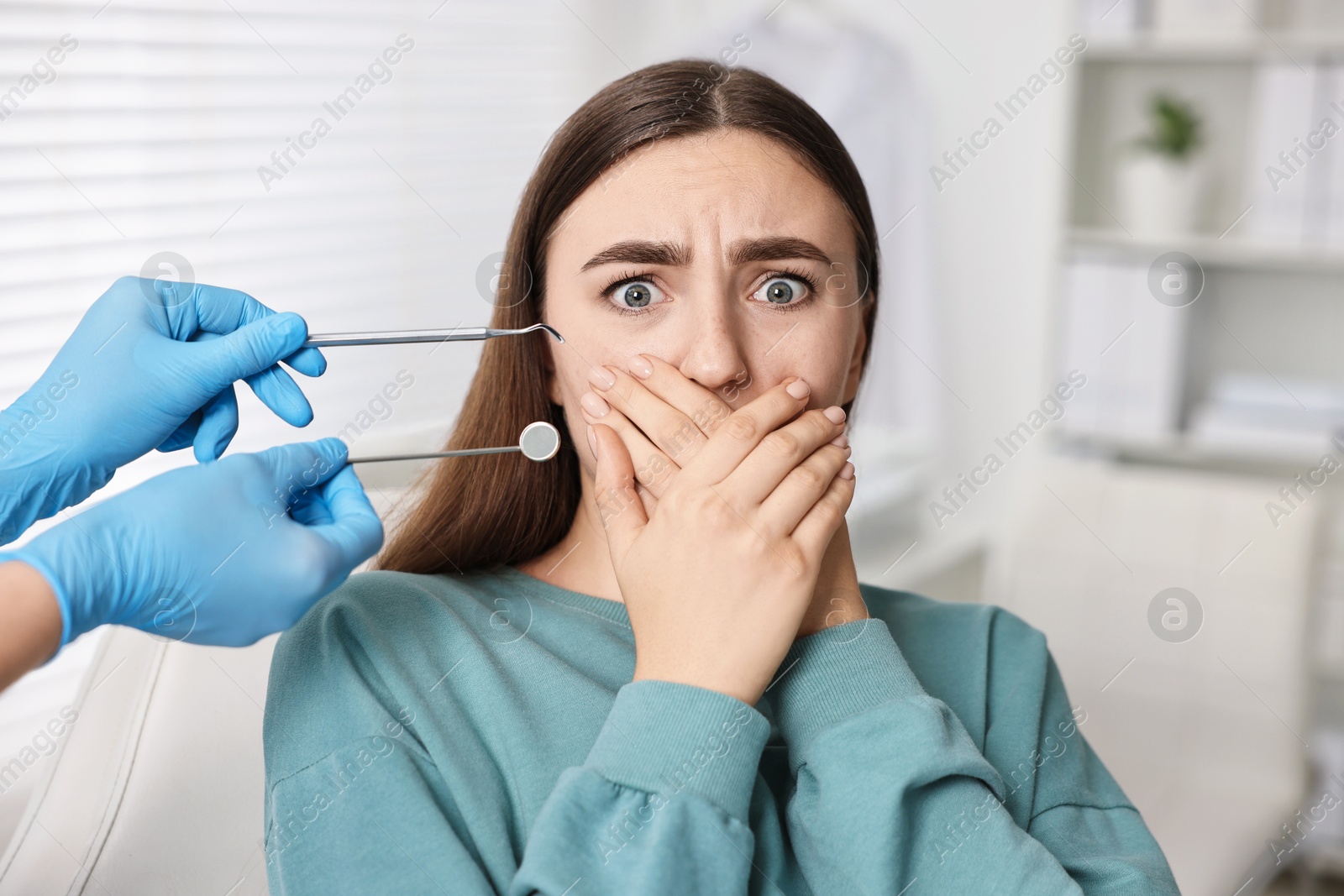 Photo of Dental phobia. Dentist working with scared woman in clinic, closeup