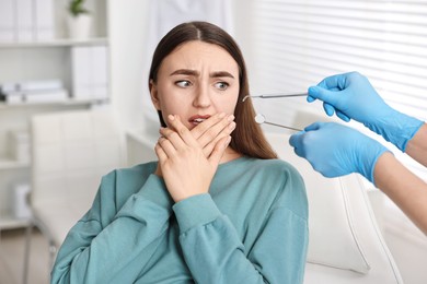 Photo of Dental phobia. Dentist working with scared woman in clinic, closeup