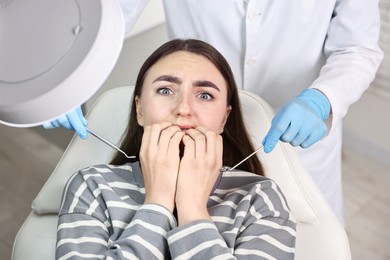 Dental phobia. Dentist working with scared woman in clinic, above view