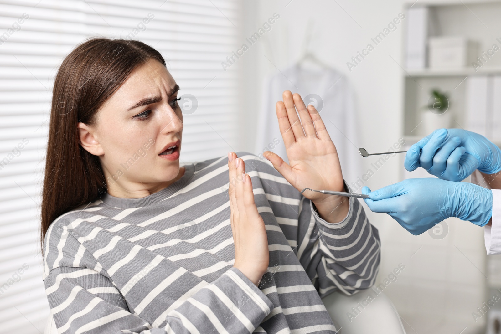 Photo of Dental phobia. Dentist working with scared woman in clinic, closeup