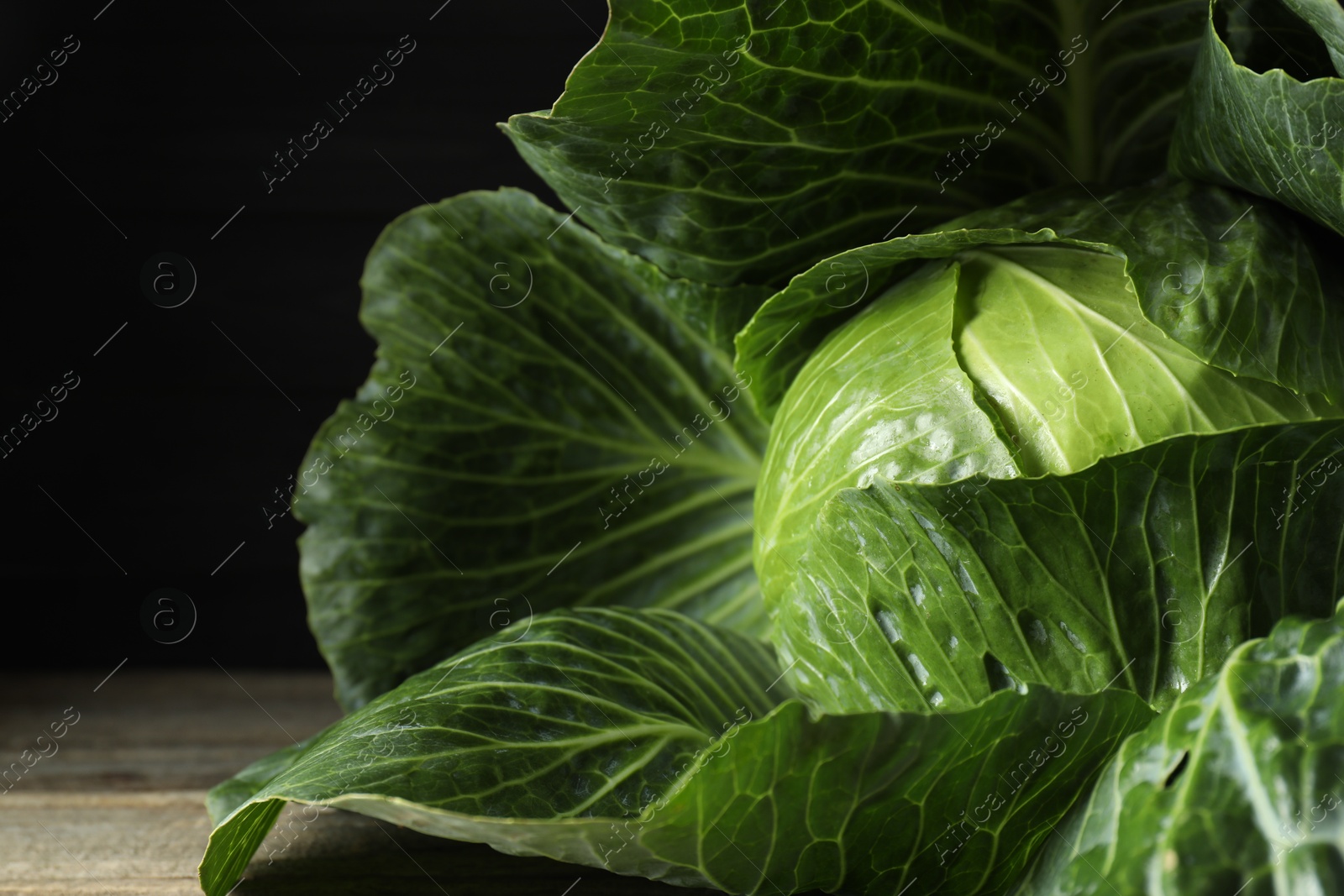 Photo of One ripe head of cabbage on wooden table against black background, closeup