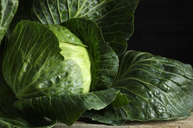 One ripe head of cabbage on wooden table against black background, closeup