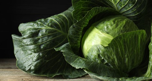 One ripe head of cabbage on wooden table against black background, closeup