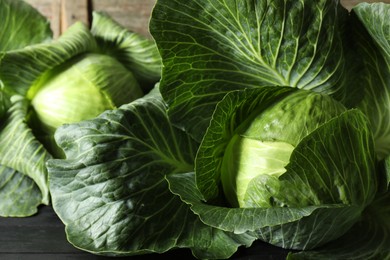 Photo of Ripe cabbages on black wooden table, closeup