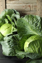 Photo of Ripe cabbages on black wooden table, closeup